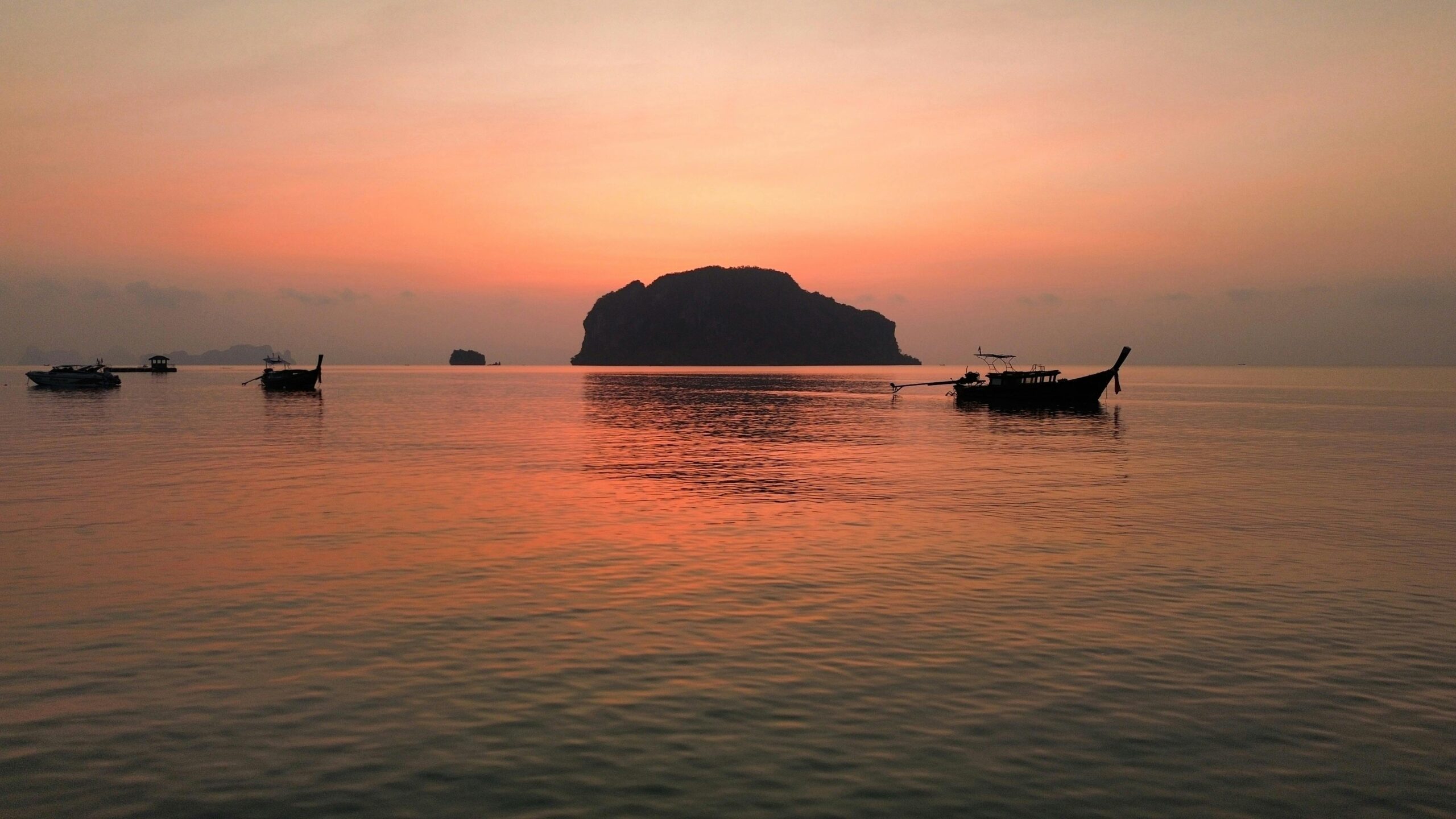 Peaceful sunrise over Phang Nga Bay in Thailand with silhouetted boats and islands.